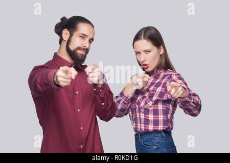 Hey you. Portrait of serious bearded man with black collected hair and woman in casual style standing and pointing at camera with serious face. indoor Stock Photo