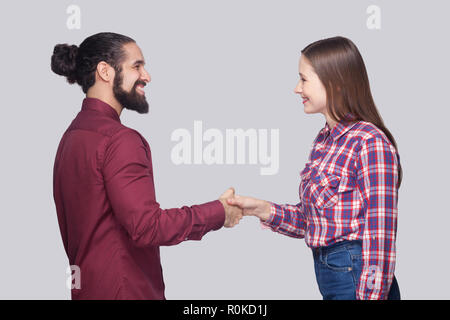 Profile side view portrait of happy bearded man with black collected hair and woman in casual style standing and shaking their hands with toothy smile Stock Photo