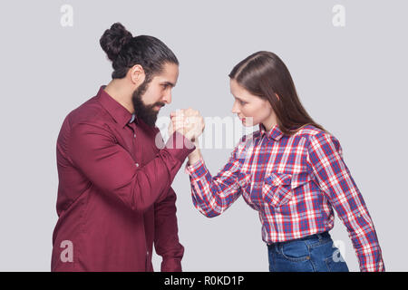 Profile side view portrait of bearded man and woman in casual style standing in armwrestling pose and looking at each other with serious face. indoor  Stock Photo