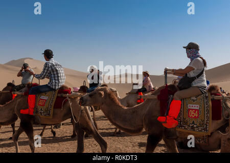 Dunhuang, China - August 8, 2012: Group of Chinese tourists riding camels at the Echoing Sand Mountain near the city of Dunhuang, in the Gansu Provinc Stock Photo