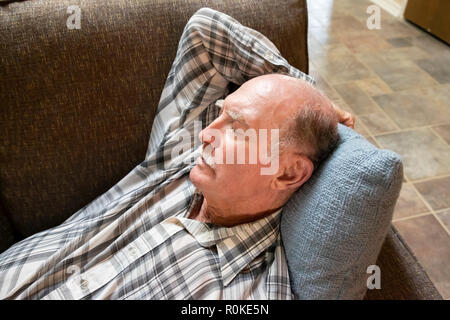 An old man wearing a plaid shirt taking a nap on a sofa. Stock Photo