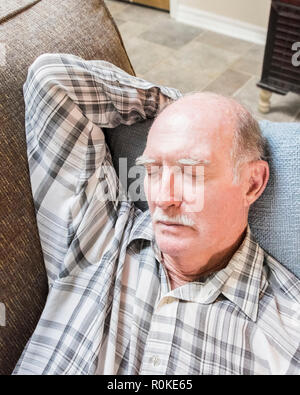 An old man wearing a plaid shirt taking a nap on a sofa. Stock Photo