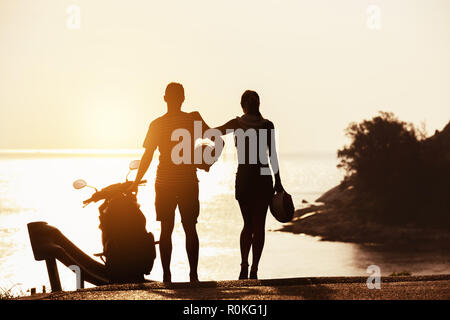 Couple's silhouettes stands with motorcycle against sunset sea bay Stock Photo