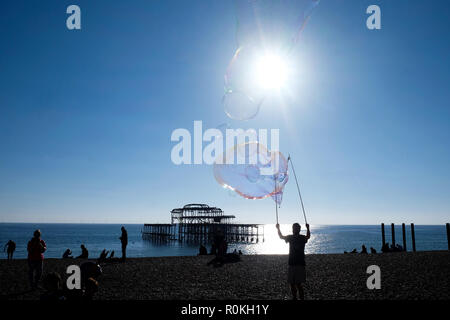 A silhouetted man standing on brighton beach with a bubble wand a big big bubble from the wand is floating in the sky, behind is Brighton’s West Pier, Stock Photo