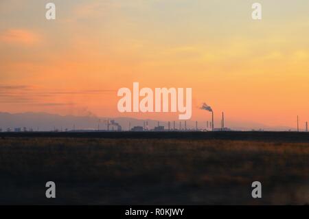 Autumn landscape with metallurgical plant with heavy smoke from pipes behind a field covered with dry grass during spectacular colorful sunset Stock Photo