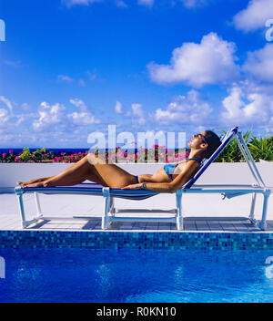 Young woman with blue bikini sunbathing on sun lounger at poolside, swimming pool, Guadeloupe, French West Indies, Stock Photo