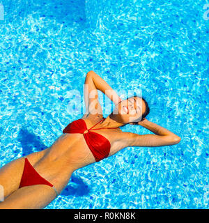 Young woman with red bikini floating on water in swimming pool, Guadeloupe, French West Indies, Stock Photo