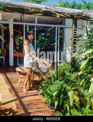 Young woman watering plants, house terrace, tropical garden, Guadeloupe, French West Indies, Stock Photo