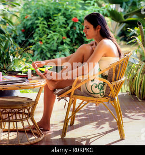 Young woman applying nail varnish on her toenails, tropical garden, Guadeloupe, French West Indies, Stock Photo