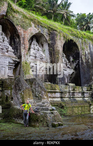 Back view of a man standing alone in front of ancient sacred royal tombs Gunung Kawi. Man is dressed traditional sarong and white top. Nobody around.  Stock Photo