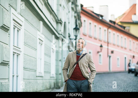 A mature businessman walking on a street in Prague city, hands in pockets. Stock Photo