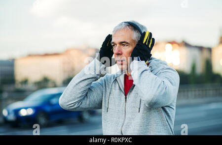 Mature male runner putting on headphones outdoors in city. Stock Photo