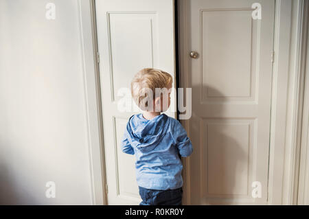 A rear view of toddler boy standing near door inside in a bedroom. Stock Photo