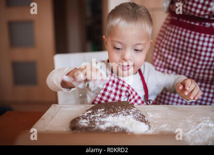 A handicapped down syndrome child with his mother indoors baking. Stock Photo