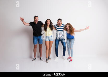 Portrait of joyful young group of friends standing arm in arm in a studio. Stock Photo