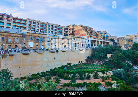 The quarters of residential buildings and hotels stretch along the hilly Sant' Antnin street of Ghajnsielem, Gozo, Malta. Stock Photo