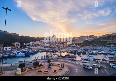 GHAJNSIELEM, MALTA - JUNE 15, 2018: The waters of Mgarr Harbour reflect the bright fiery sunset and illuminate the boats in its colors, on June 15 in  Stock Photo