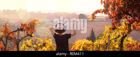 Girl in a hat at sunset and a glass of wine in hand. Nature Italy, hills and grape fields the sunlight. Glare and sun rays in the frame. Free space for text. Copy space. Stock Photo