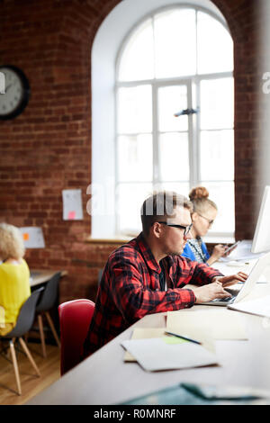 Some managers co-working while sitting by table and using modern gadgets Stock Photo