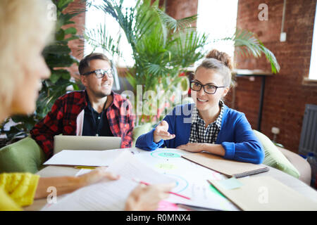 Young successful businesswoman having working conversation with one of colleagues at meeting Stock Photo