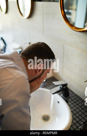 Tired or sleepy businessman refreshing with cool water over sink in bathroom of airport Stock Photo