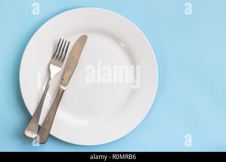Dinner plate, knife and fork isolated on blue backgroud Stock Photo