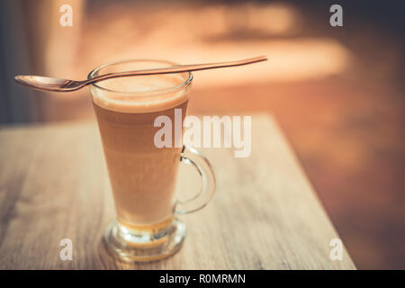 Relaxing morning closeup, coffee on wooden table top in long glass. Latte for morning motivation and day start Stock Photo