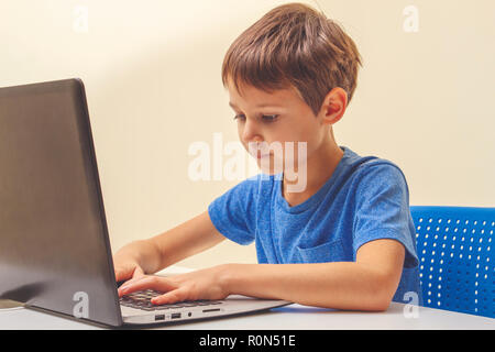 Concentrated boy sitting at desk with laptop computer and doing homework Stock Photo