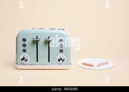 Retro green four slice double toaster on a vintage tan background with a slice of bread on a white plate ready to be toasted with copy space Stock Photo