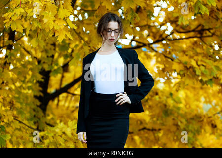 Business woman in formal wear stands over yellow autumn trees. Stock Photo