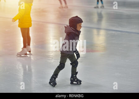 Adorable little boy in winter clothes with protections skating on ice rink Stock Photo