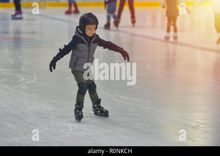 Adorable little boy in winter clothes with protections skating on ice rink Stock Photo