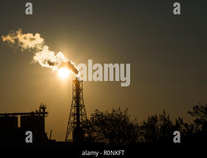 Factory chimney emits or discharges heavy smokes during sunset creating pollution. Stock Photo