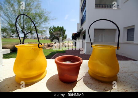 Small yellow and terracotta pots, on a stone ledge, with bright background of a golf course and apartments Stock Photo
