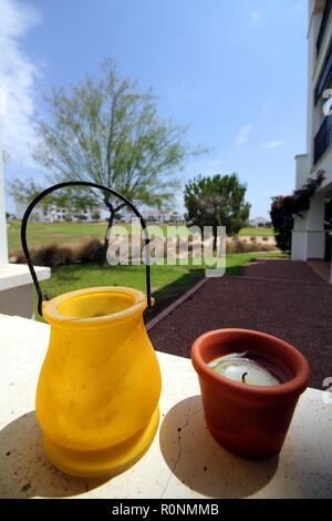 Small yellow and terracotta pots, on a stone ledge, with bright background of a golf course and apartments Stock Photo