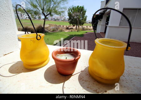 Small yellow and terracotta pots, on a stone ledge, with bright background of a golf course and apartments Stock Photo