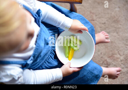 Young baby toddler girl aged two years old eating healthy diet of fresh peppers and cucumbers snack Photograph taken by Simon Dack