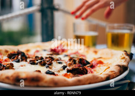 Aubergine pizza on a table and a woman's hand reaching for a beer Stock Photo