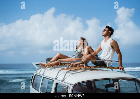 young couple with sunglasses sitting on top of minivan roof Stock Photo