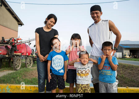 Portrait of smiling Japanese farmer, his wife and four children standing in their yard, children pulling faces at camera. Stock Photo