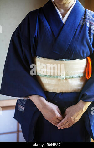 Close up of Japanese woman wearing traditional bright blue kimono with cream coloured obi kneeling on floor.