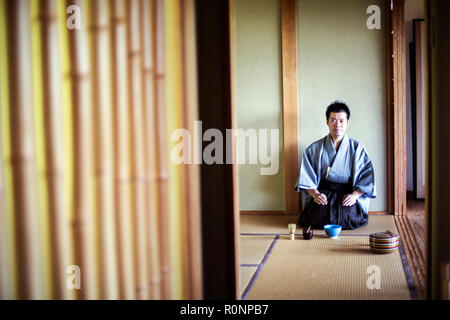 Japanese man wearing traditional kimono kneeling on tatami mat during tea ceremony. Stock Photo