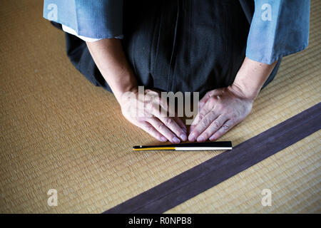 High angle close up of Japanese man kneeling on tatami mat in front of Sensu fan during a tea ceremony, used as a greeting. Stock Photo