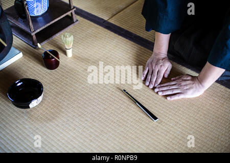 High angle close up of Japanese man kneeling on tatami mat in front of Sensu fan, bowl and whisk used in tea ceremony. Stock Photo