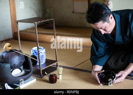 Japanese man wearing traditional kimono kneeling on floor, holding tea bowl, during tea ceremony. Stock Photo