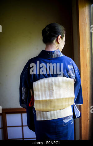 Rear view of Japanese woman wearing traditional bright blue kimono with cream coloured obi.
