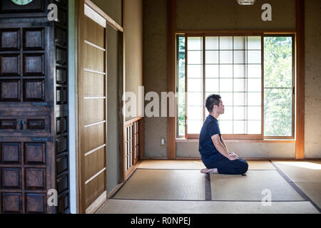 Japanese man kneeling on tatami mat in traditional Japanese house. Stock Photo