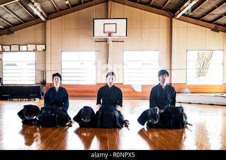 Female and two male Japanese Kendo fighters kneeling on wooden floor, meditating. Stock Photo