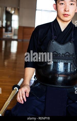 Female Japanese Kendo fighter kneeling on wooden floor, fastening Kendo  mask. Stock Photo
