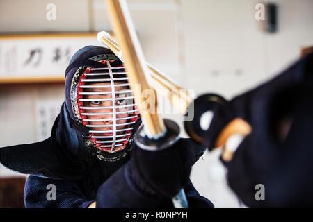 Female Japanese Kendo fighter kneeling on wooden floor, fastening Kendo  mask. Stock Photo